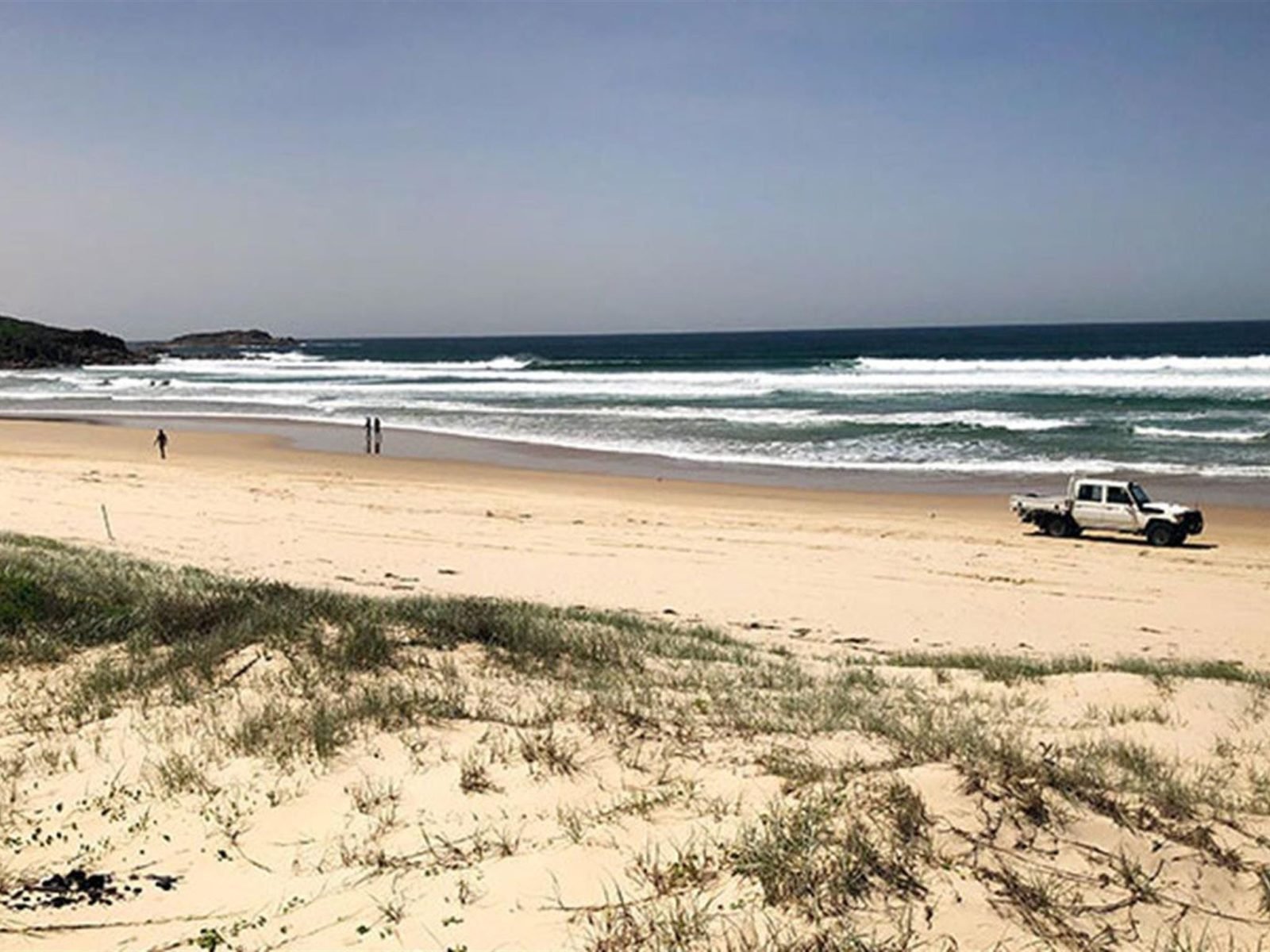 View across dunes to people and a vehicle on Samurai Beach and a distant headland. Photo: Jim Cutler