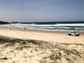 View across dunes to people and a vehicle on Samurai Beach and a distant headland. Photo: Jim Cutler
