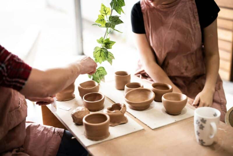 picture shows two people seated at a bench with a board of clay pots between them