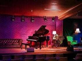 a picture of a stage, lit with rose coloured lights onto a brick background, with black grand piano