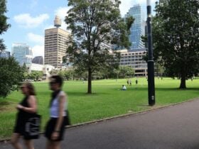 A park with lush green grass and two people walking on a path