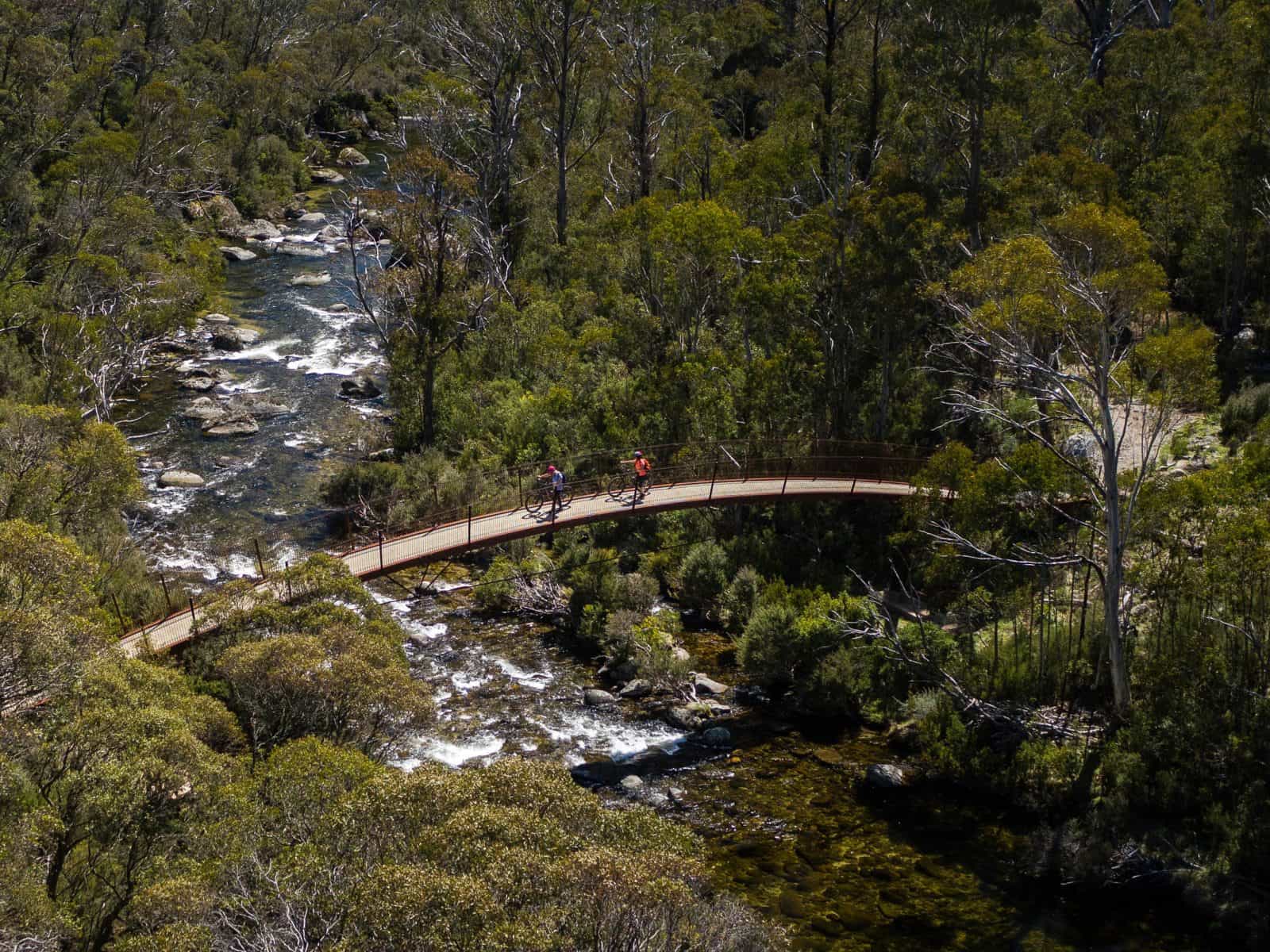 Aerial view of two bike riders crossing a bridge on Thredbo Valley track, Kosciuszko National Park
