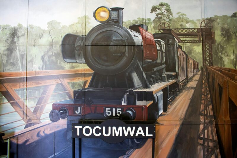 Mural of steam engine crossing bridge, with a railway station sign saying 