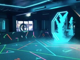 A large, open-plan room with geometric markings on walls and floor, dimly lit with green LED lights.