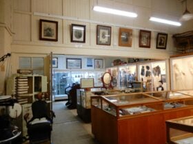 Large room with many display cases containing historical items such as dress, portraits and more.