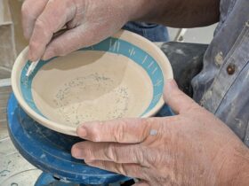 a pair of hands decorating a pottery bowl
