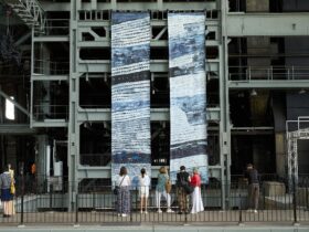 people standing on a balcony looking at two large paintings hanging from in a power station