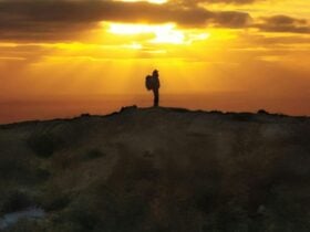 Woman on cliff with sun golden sun behind her