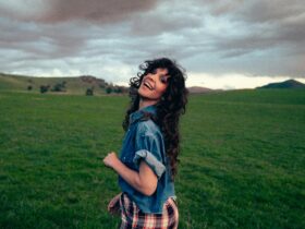 Smiling woman looking over her shoulder, lush green rolling hills & stormy sky in background
