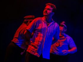 A man in red and blue lighting, his arms held behind him by two police officers.