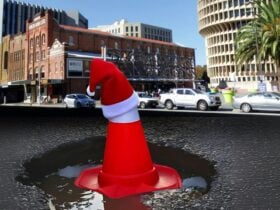 A picture of a traffic cone sitting in a pothole with a santa hat on