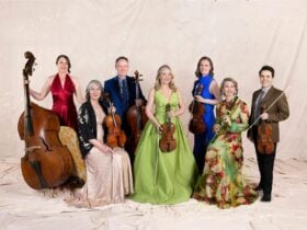 Seven people standing with their classical musical instruments, wearing formal suits and ballgowns