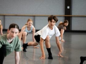 Young male (aged ~ 16-18) is dancing in a crouched position. There are other dancers around him.
