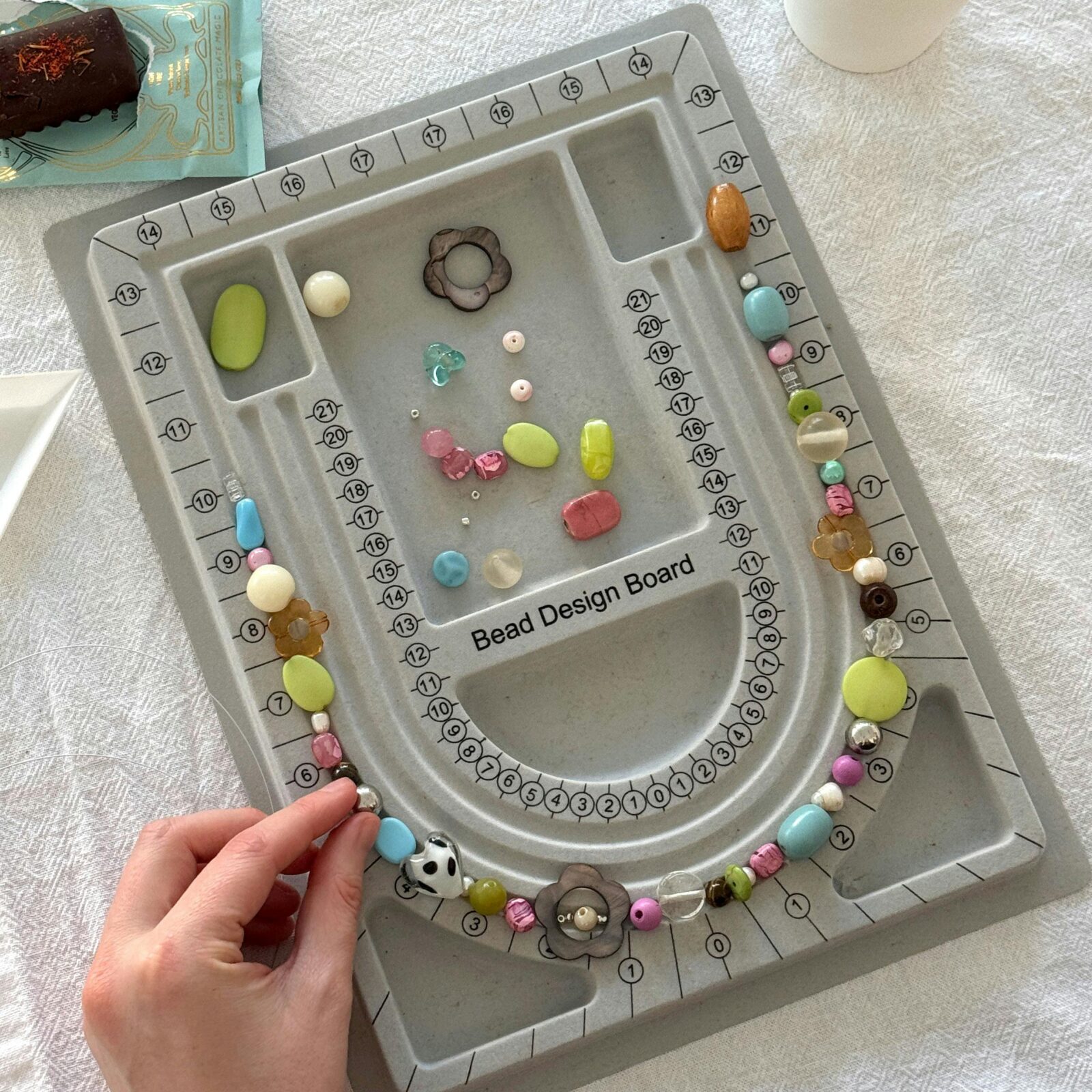 A grey bead design board on a table with hands reaching in moving beads around