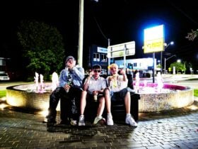 Three young men sitting in front of a fountain at night recreating the friends intro