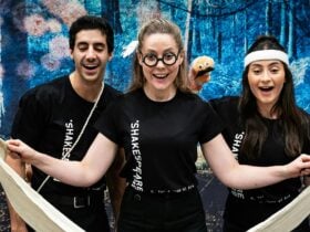 Three Bell Shakespeare actors smile with props in front of a whimsical forest backdrop.