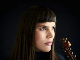 Close up of Benedicte, who holds a violin. Black backdrop