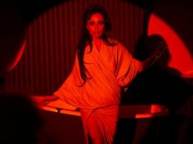 A mysterious femme fatale with piercing gaze under red stage lights.