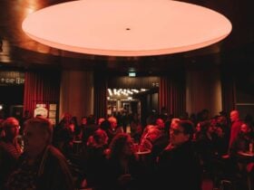 A dimly lit bar or lounge filled with people socializing under a large, circular red ceiling light.