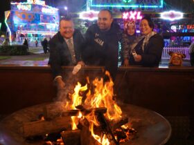 Three People standing in front of a large fire pit toasting Marshmallows