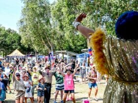 A person in a glamourous boa waving to a crowd of families with children, adults and elderly people