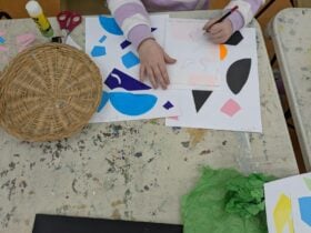 A young child creates a collage with coloured paper shapes and pencils