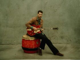 Ernest aines sitting on drum holding electric guitar