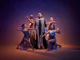 Four dancers in costume pose around Composer William Barton in the centre