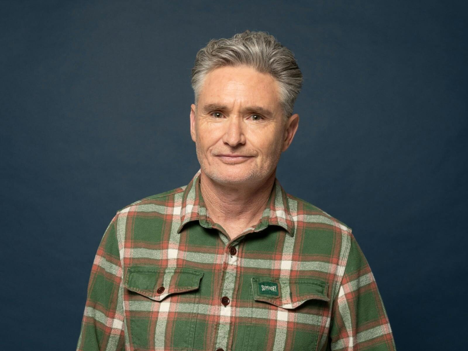 Comedian Dave Hughes standing in front of a dark background