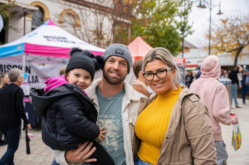 A man and woman standing next to each other smiling, the man is holding a young child.