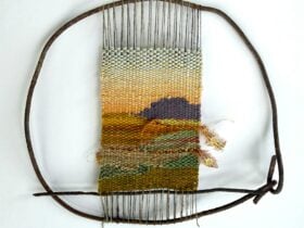 A woven tapestry of a sunset, held within a circular wire frame