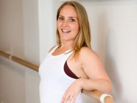 A bright happy pilates instructor with honey blonde hair and white singlet top smiling
