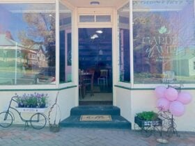 Street view of shop with 2 bay windows and recessed door. Door is open to welcome guests.