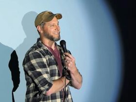 Comedian Jimmy Kuratz on stage in the spotlight against a light blue backdrop.