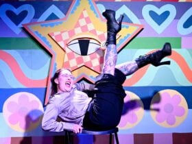 A woman in front of a star decal background, on the floor with legs in the air and laughing