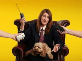 A woman sits in a brown leather armchair against a yellow backdrop with a dog and hands with items