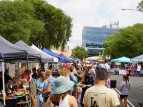 A large group of people are walking through the market looking at the stalls