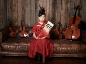 One female sitting on a couch, holding a violin. There are two violins by each side.