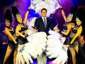 Imag of a man surrounded by women holding large feathered fanss