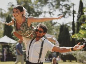 Two dancers dressed in jazz-style. The lady is on the man's right shoulder with her arms out.