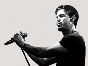 A man with a black t-shirt standing holding a microphone, looking to the left of camera