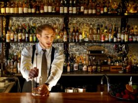 A performing bartender crafts a cocktail behind the bar while talking to the audience