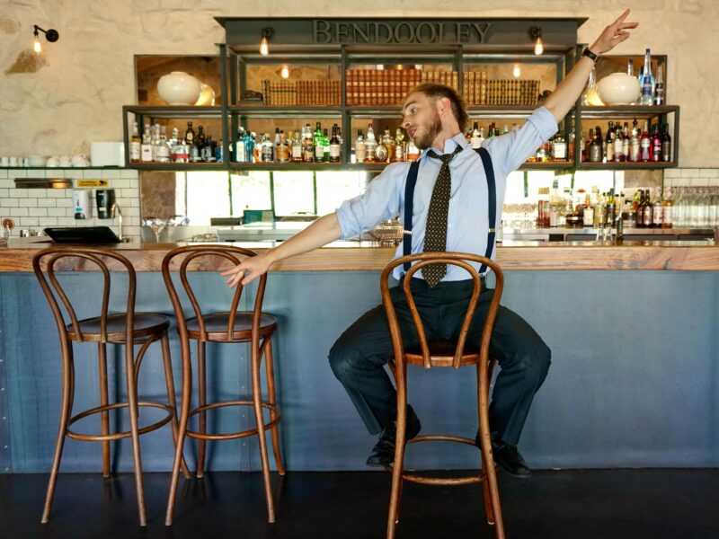 A performing bartender dances like Frank Sinatra on a stool in front of the bar