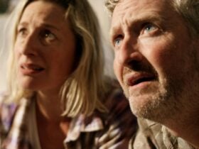 A man and woman looking up towards the sky with sunlight on their worried faces