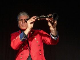 A man dressed in a red suit looking through a telescope.