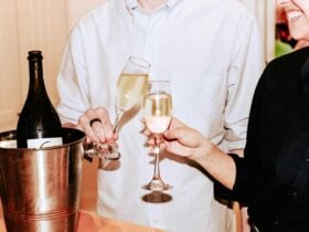 Glass of champagne poured into a pair of glasses with a two people clinking the glasses.