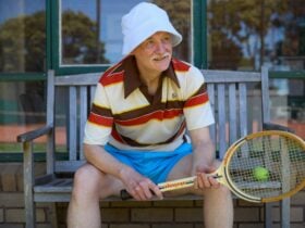 A man seated on a bench holding a tennis racquet dressed in sports clothes
