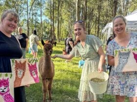 2 ladies holding their completed painting to compare with a real alpaca