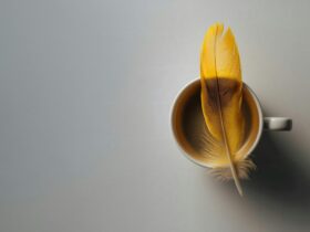 A full cup of coffee with a yellow feather sitting on top.