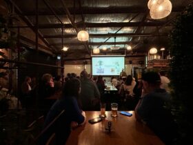 A speaker in a dark pub with a captive audience facing him.